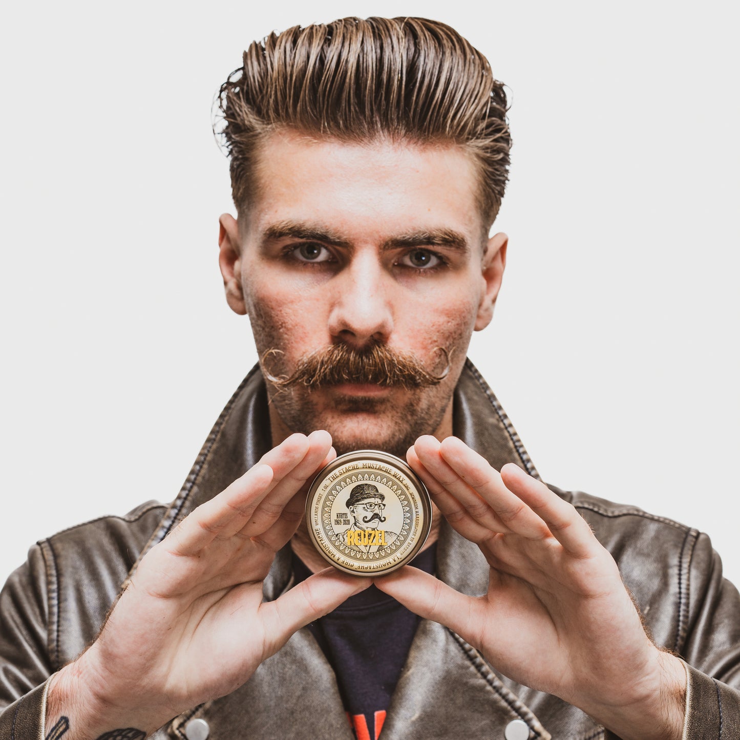 Reuzel The Stache Mustache Wax in a tin, featuring a natural mustache wax with a smooth texture and branding on the lid.